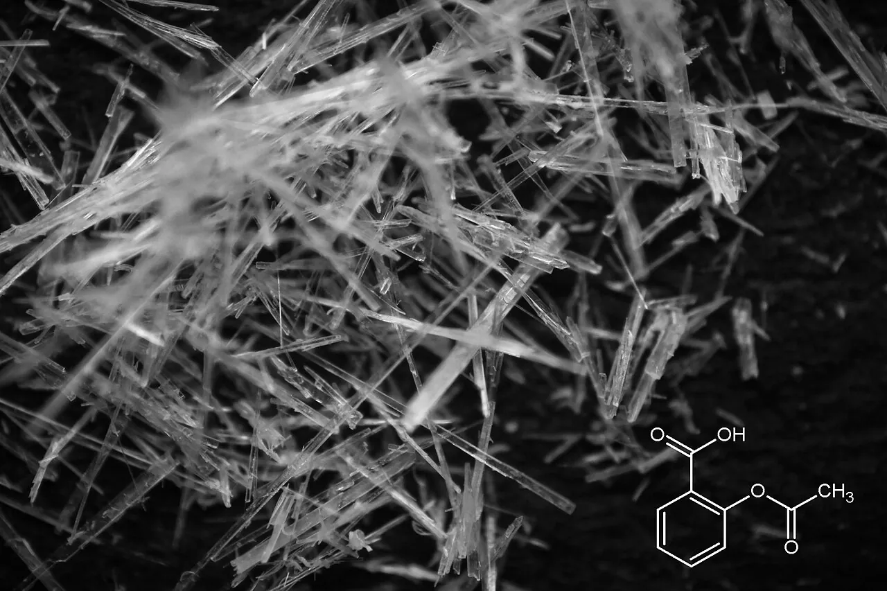 Asetilsalisilik asit (aspirin) kristallerinin makro fotoğrafı; sağ altta yapı formülü görülüyor.