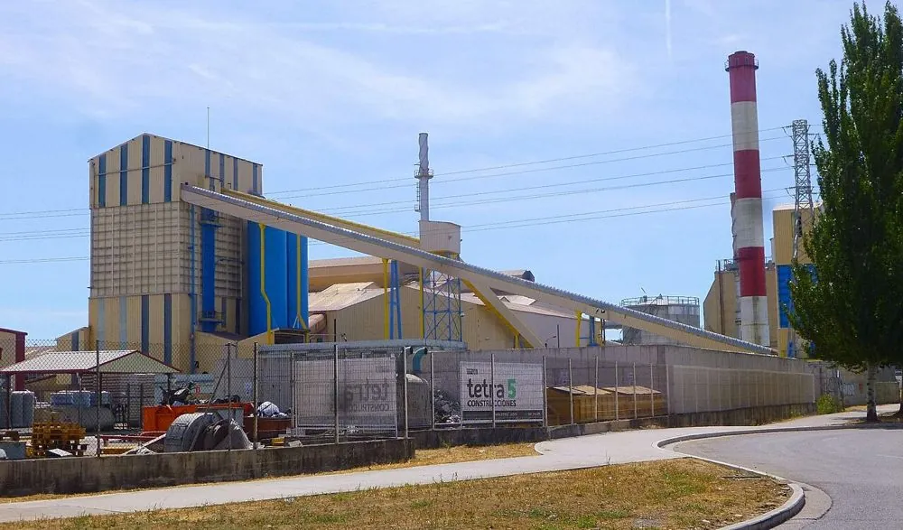 Bir cam ambalaj tesisi (Verallia, Burgos): solda harman binası ve silolar, eğimli konveyör bant, arkada fırın bacaları.