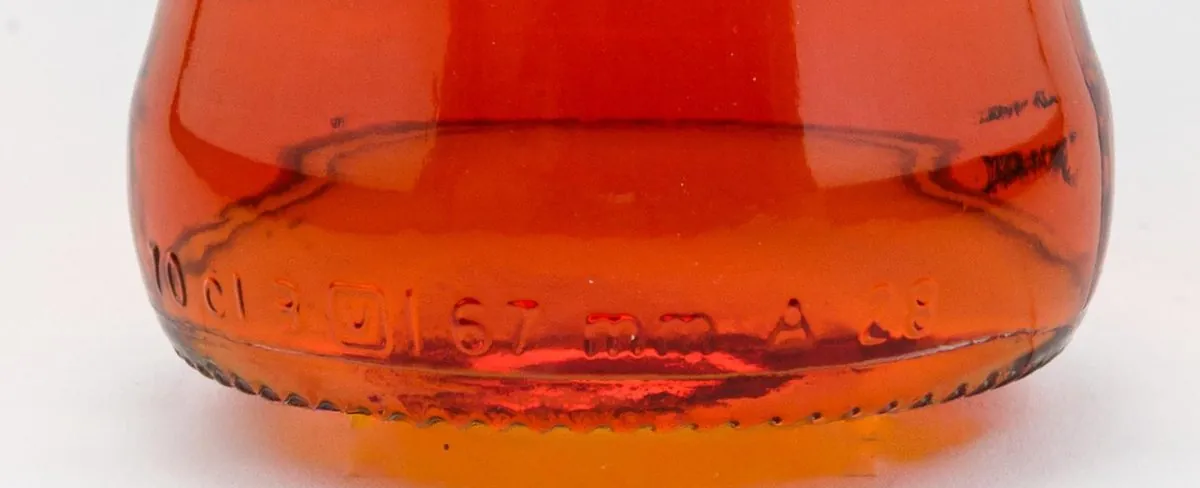 Gerçek bir şişede tabana yakın kabartmalar (Aperol, 70 cl, 2026 tasarımı). Soldan sağa okunanlar: hacim (70 cl), bir kare…